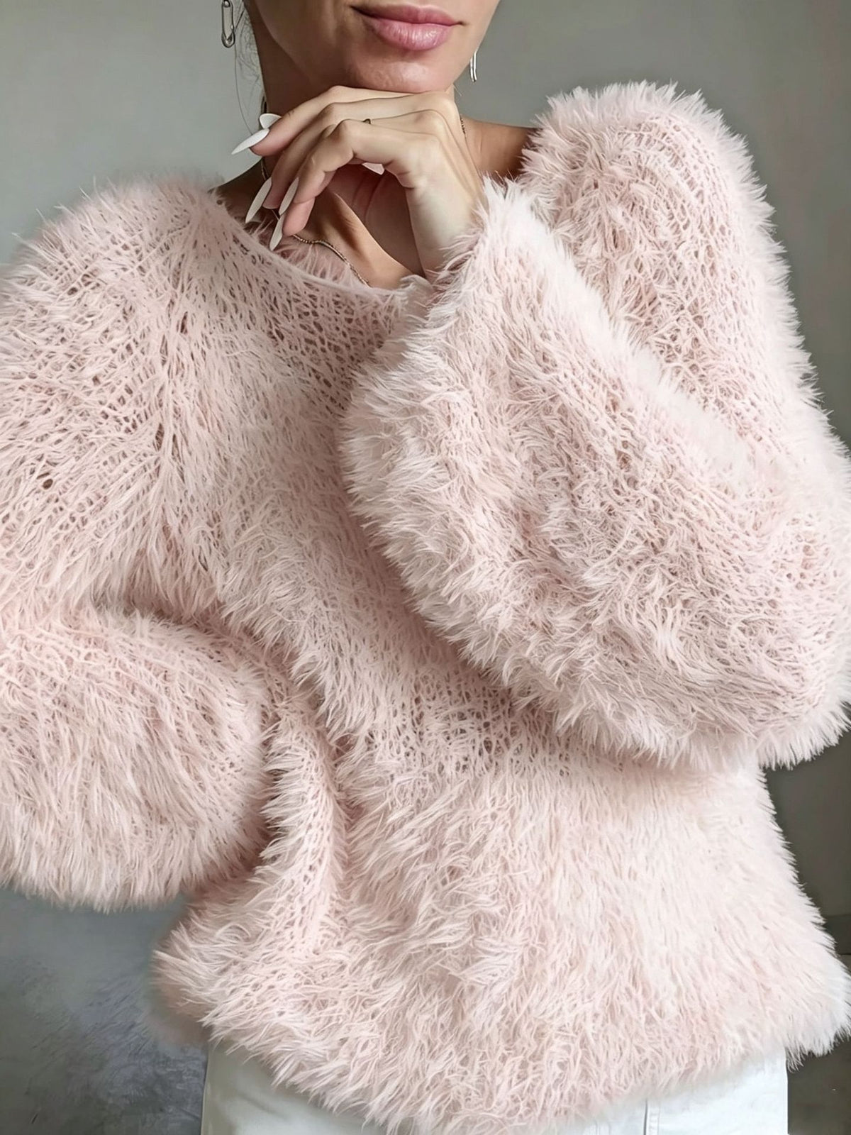 A close-up of a woman wearing a fuzzy, light pink long-sleeve knit sweater with a crew neck, paired with white pants.