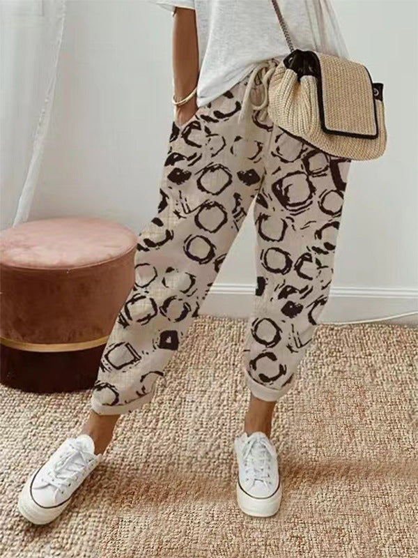 Person wearing leopard print pants with a white top and white sneakers, holding a straw bag.