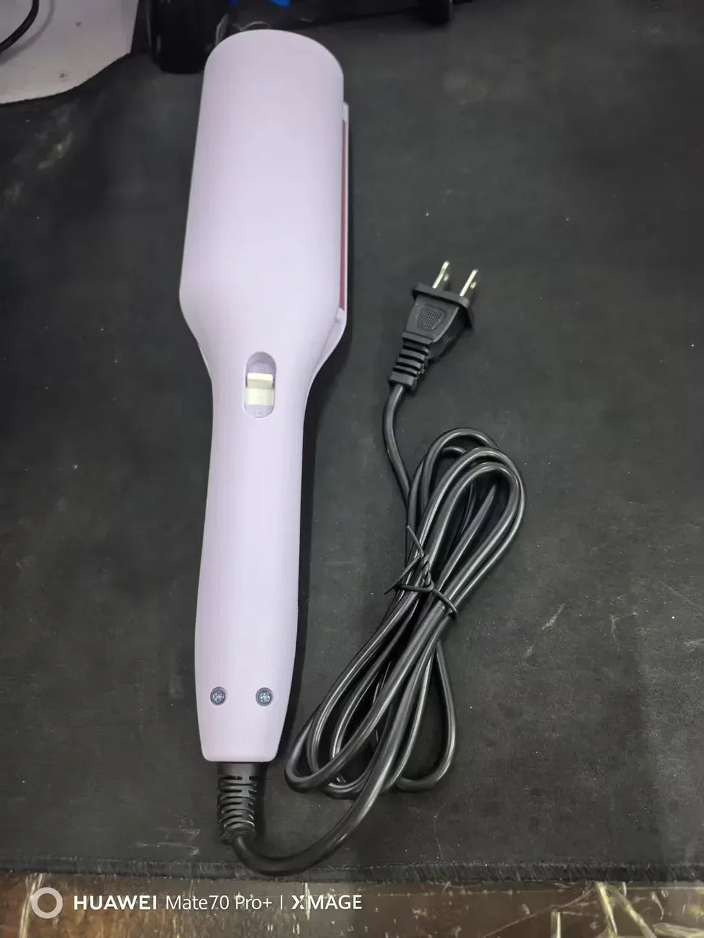 Electric hair straightener with power cord on black surface, beauty styling tool
