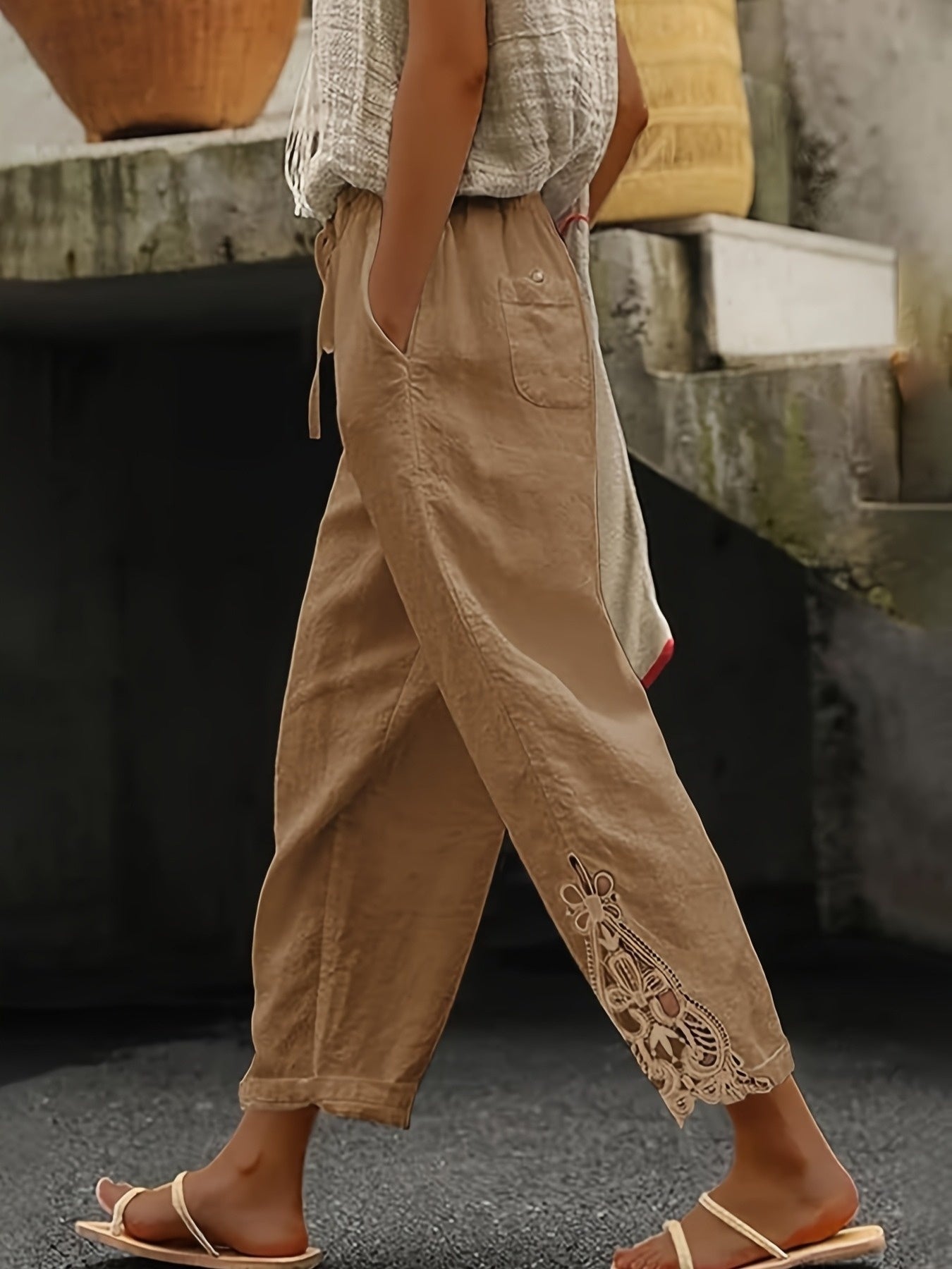 Person wearing beige pants with lace details and sandals, standing on a street.