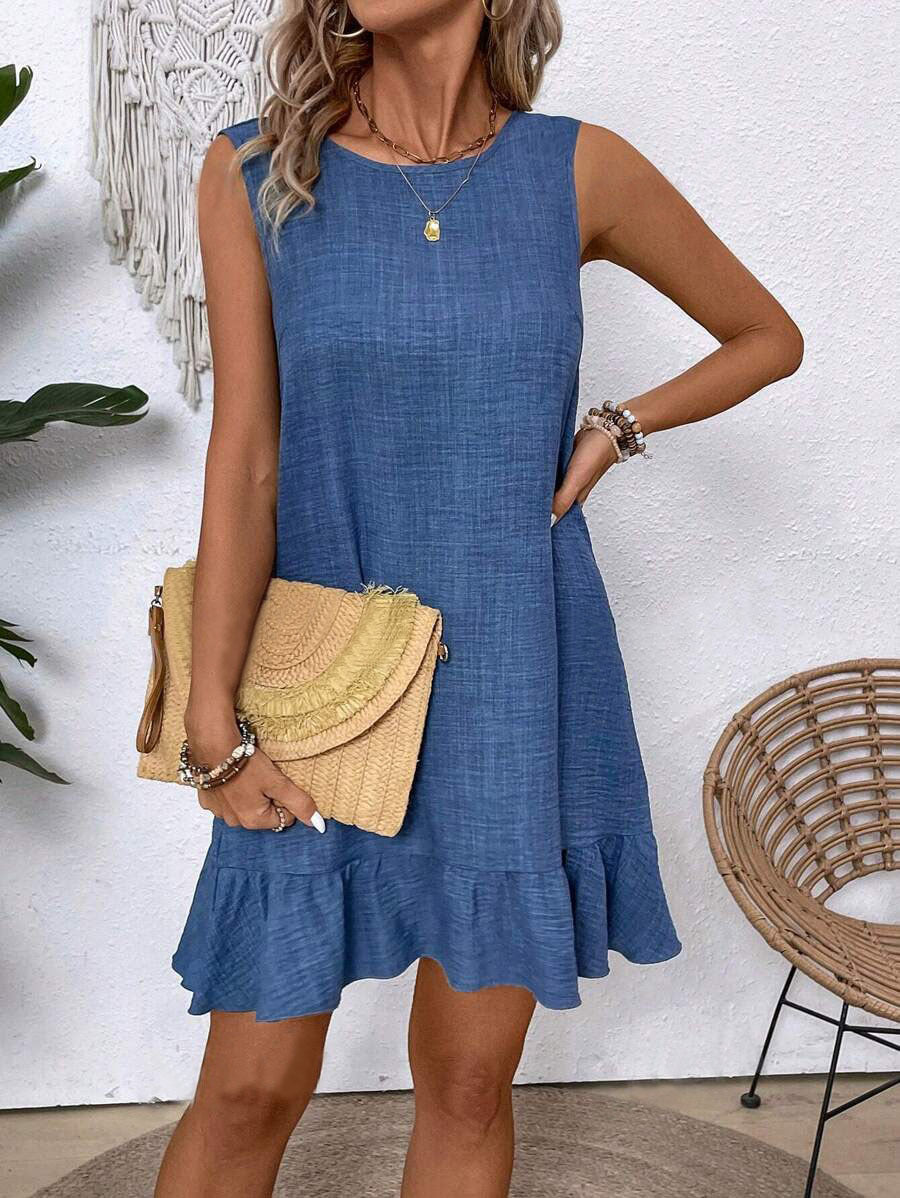 Woman wearing a blue dress holding a straw bag against a white wall.