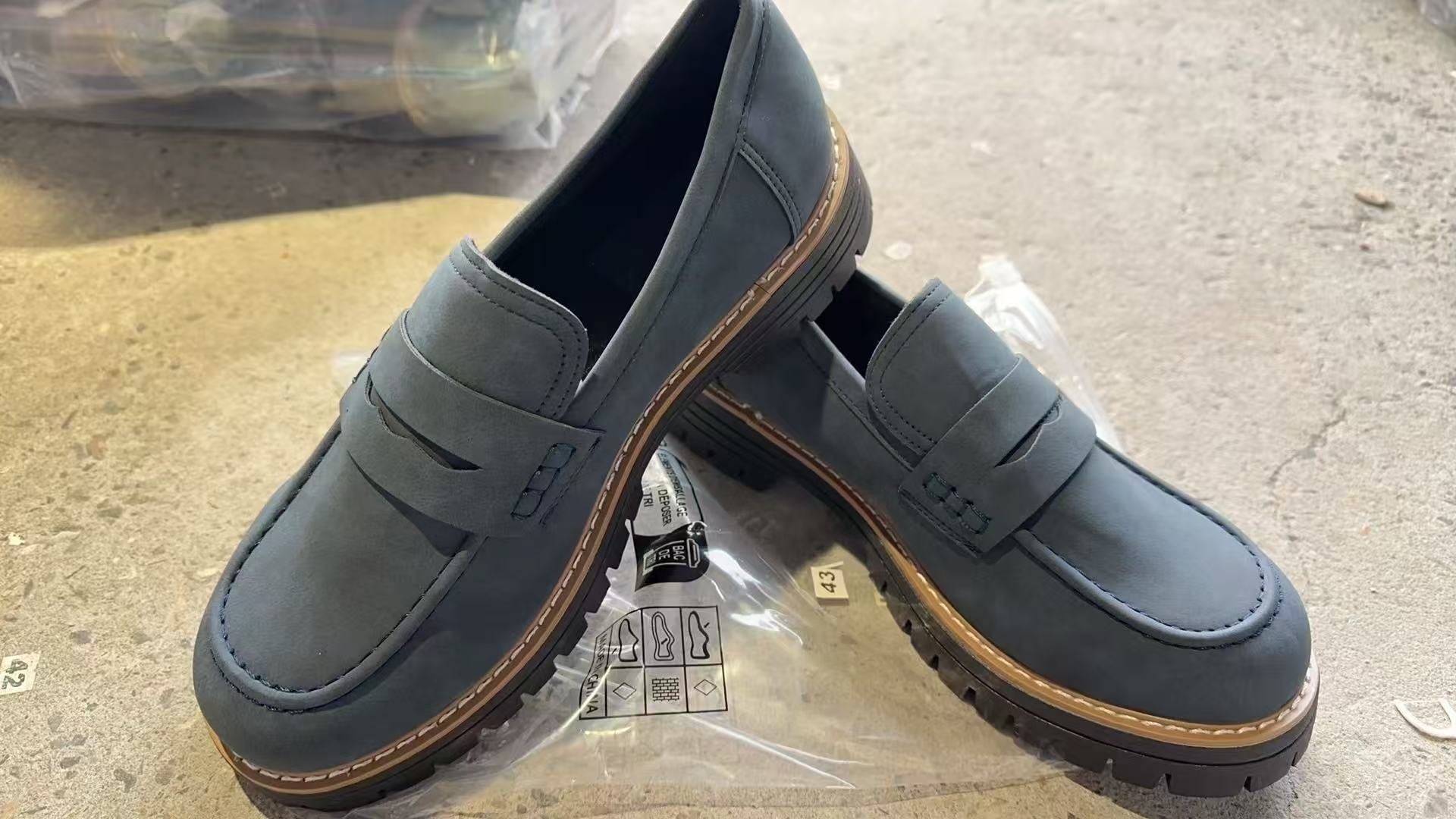 Pair of gray loafers on a concrete surface with a clear plastic bag underneath.