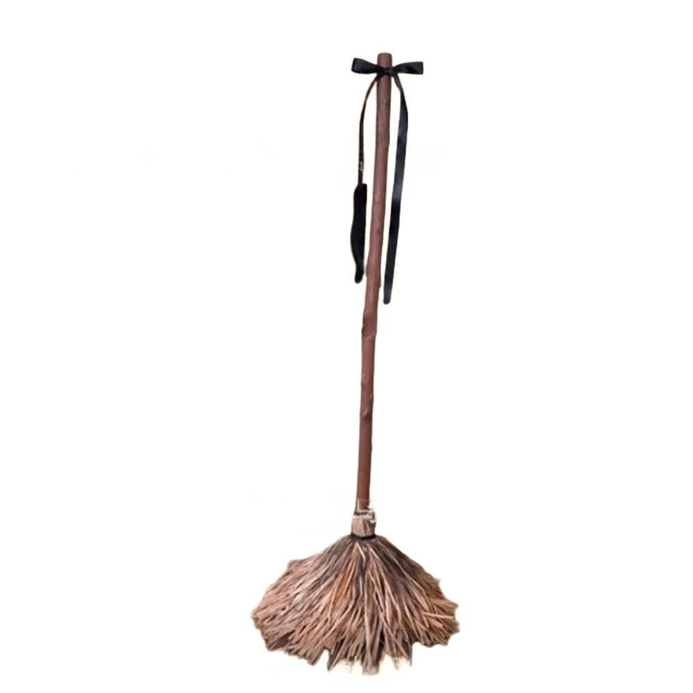 A miniature witch's broom with a brown wooden handle, straw-colored bristles, and a black ribbon tied at the top, shown against a plain white background.