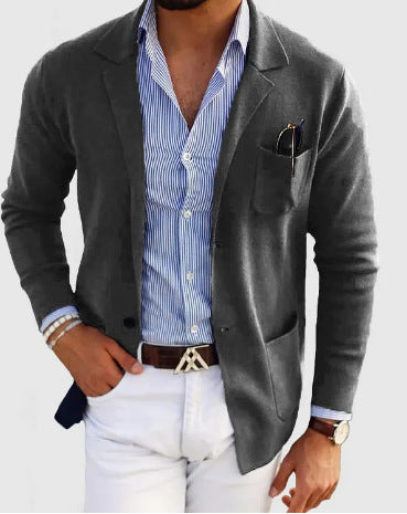Man wearing a gray blazer over a striped shirt with white pants on a light background
