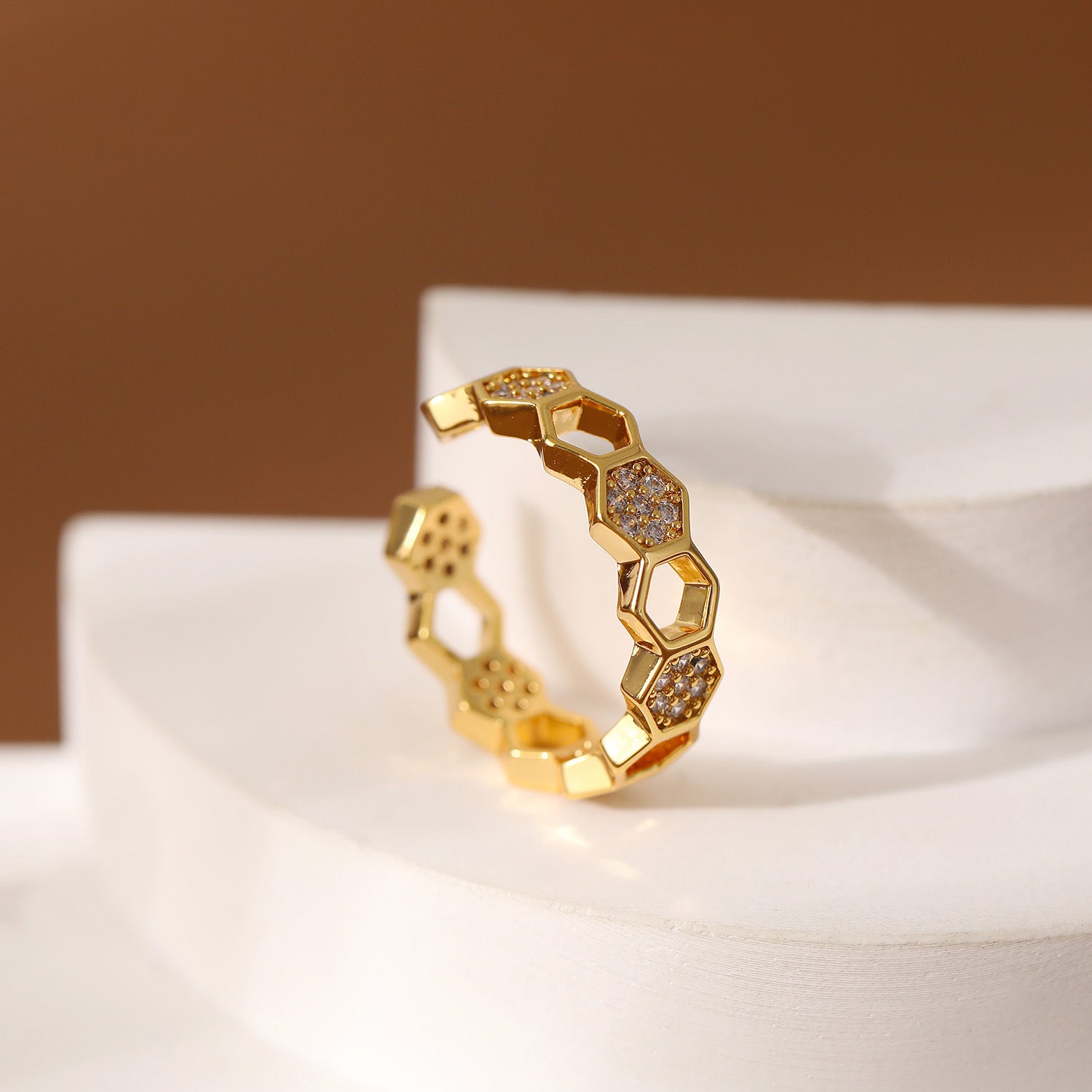 Gold ring with honeycomb design on a white surface with a brown background
