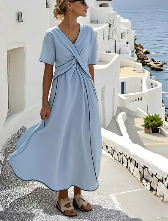 Woman in a light blue dress standing on a picturesque coastal street with white buildings and blue sea.