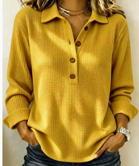 A woman wearing a mustard yellow waffle-knit long-sleeve polo shirt with a buttoned collar and three front buttons, paired with dark jeans.