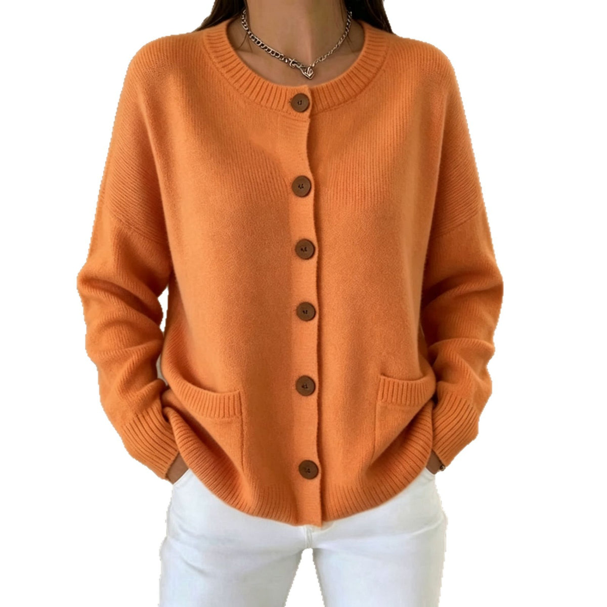A woman wearing a cozy, light orange knit cardigan sweater with brown buttons and white pants, shown from the neck down against a plain white background.