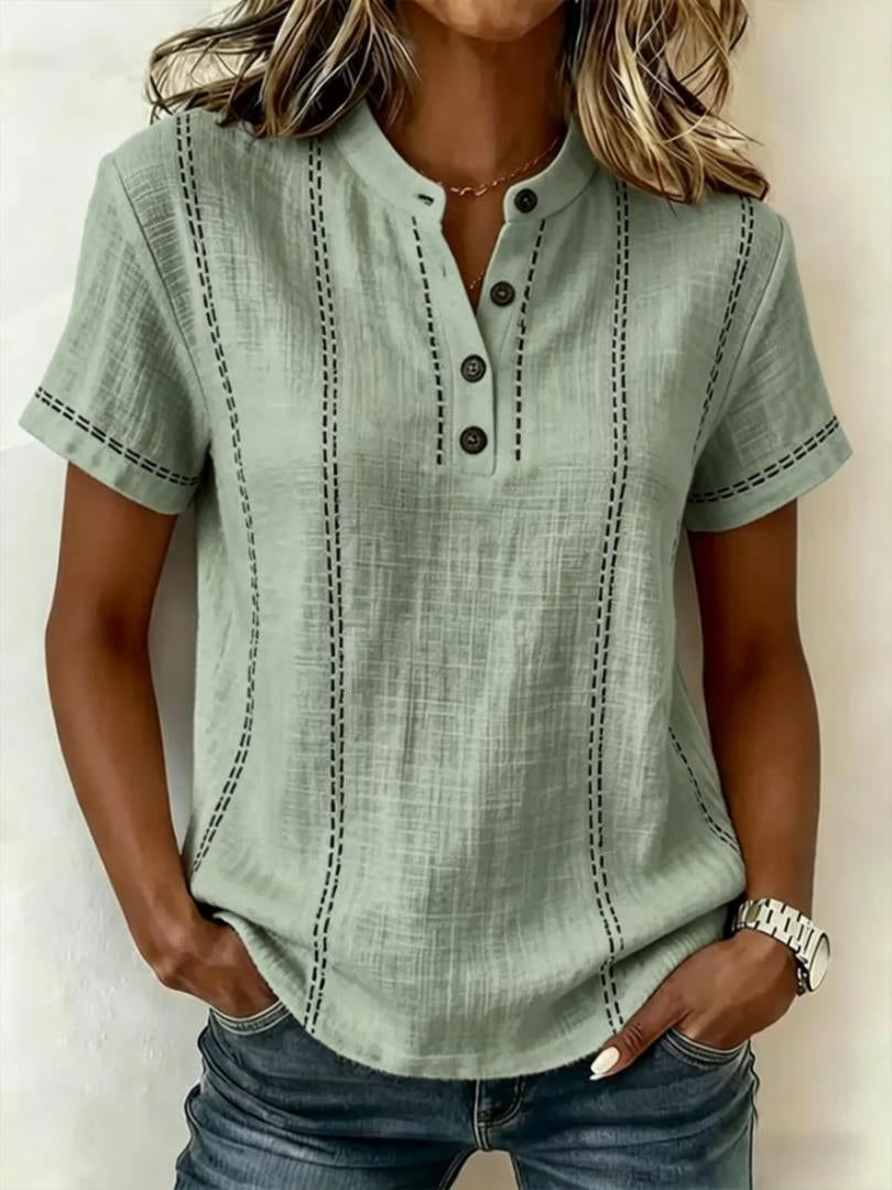 Person wearing a light green short-sleeve shirt with button details on a plain background