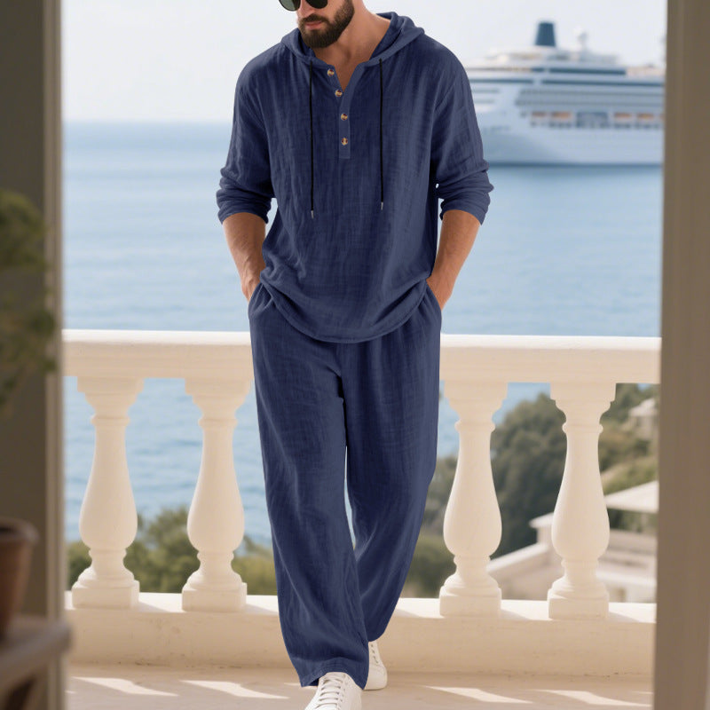 Man in navy blue outfit standing on a balcony with ocean and cruise ship in the background