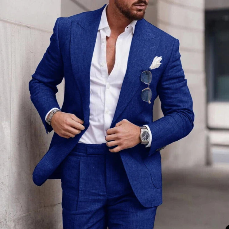 Man wearing a blue suit with a white shirt, standing against a neutral background.