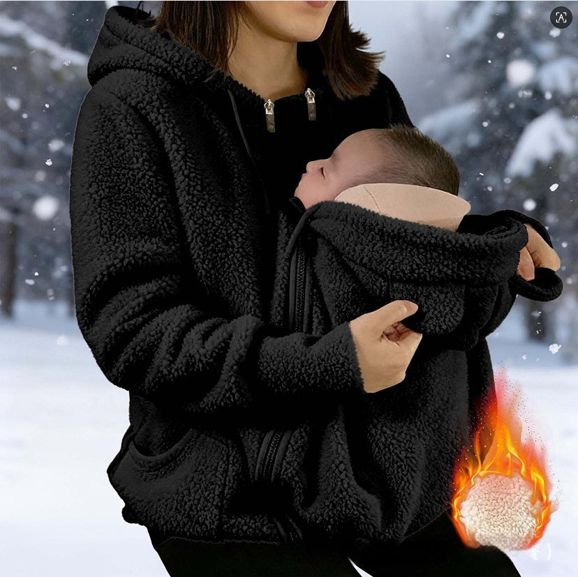 A woman in a black fleece hooded jacket holds a baby in a matching black baby carrier pouch. The background is a snowy outdoor scene with falling snow, and a flame graphic with a close-up of the fleece texture appears in the bottom right corner to emphasize warmth.