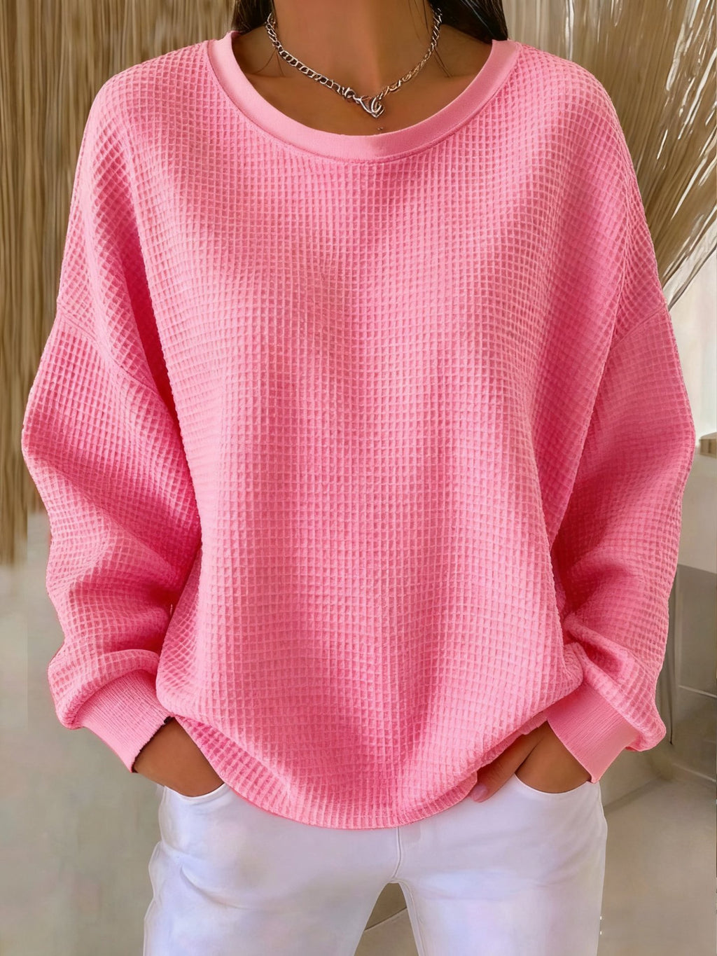Person wearing a pink textured sweater and white pants indoors.