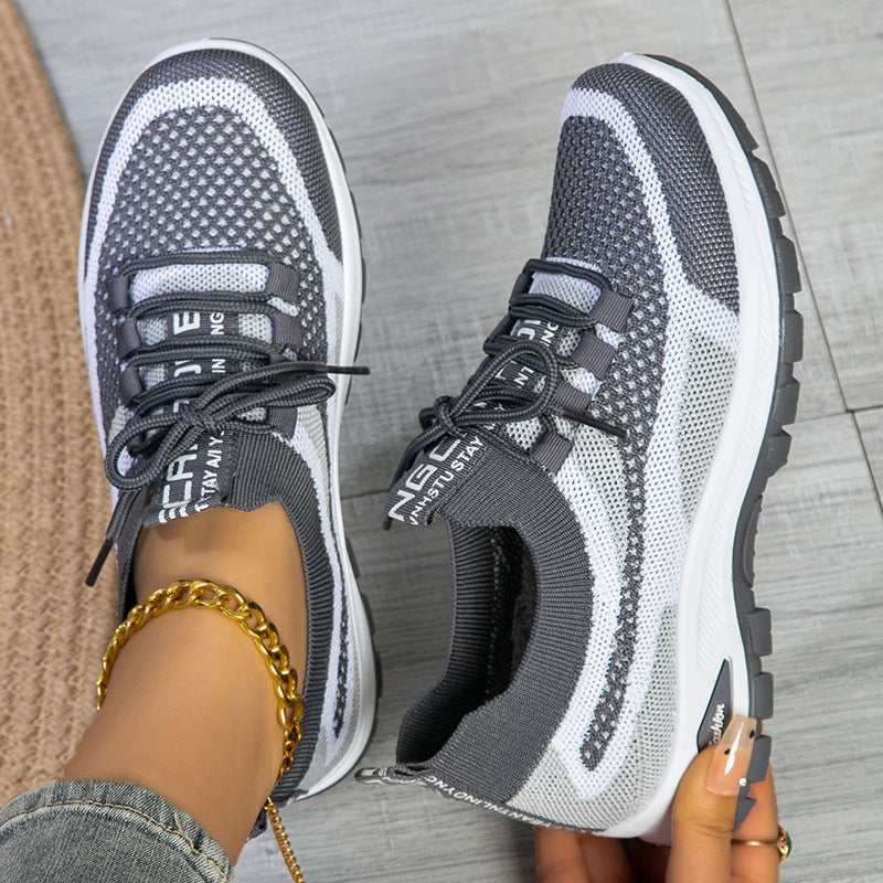 Gray and white sneakers worn on a gray floor with a gold bracelet visible.