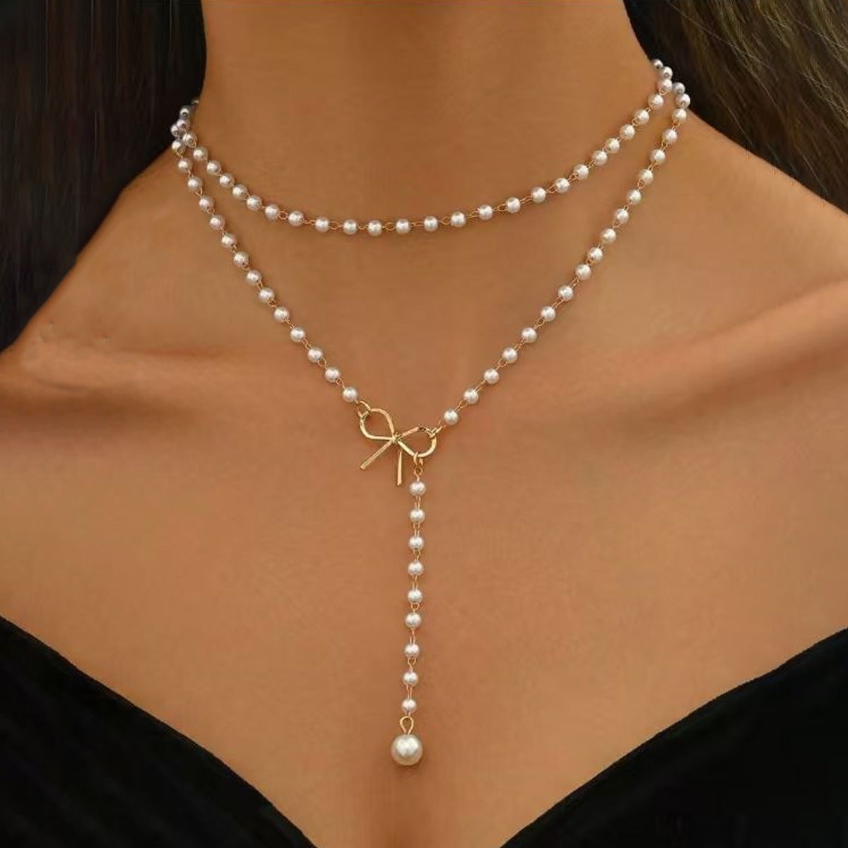 Pearl necklace with a gold bow charm on a model wearing a black top.