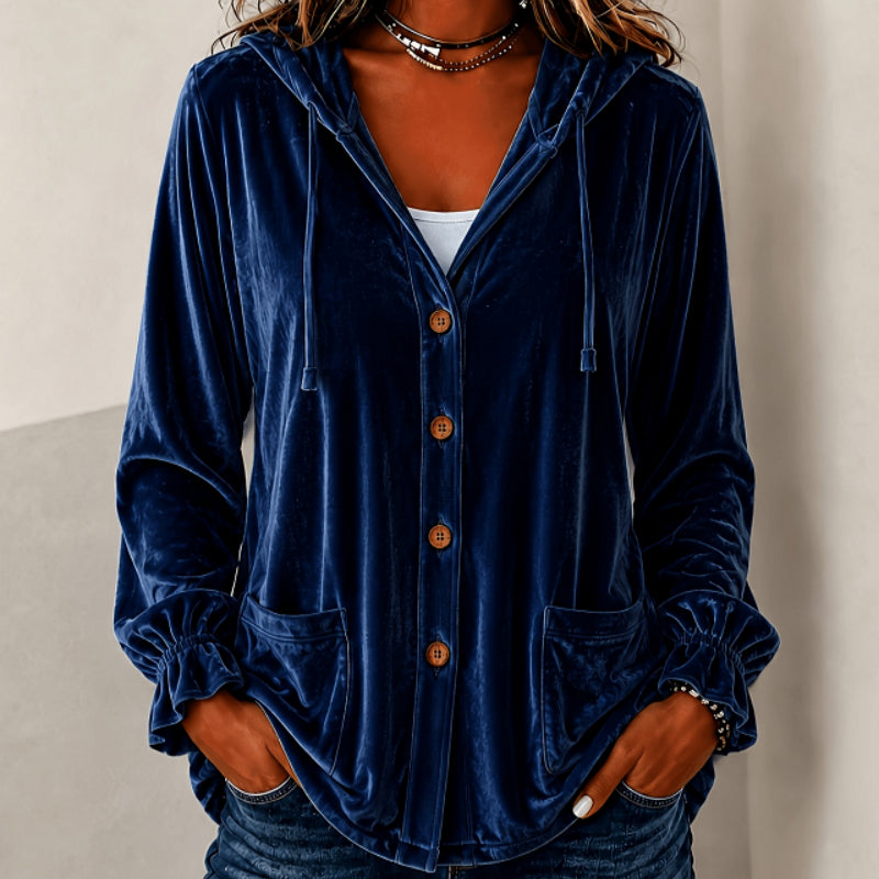 A woman wearing a navy blue velvet hooded button-up shirt with brown buttons, elasticized cuffs, and front pockets, paired with blue jeans.