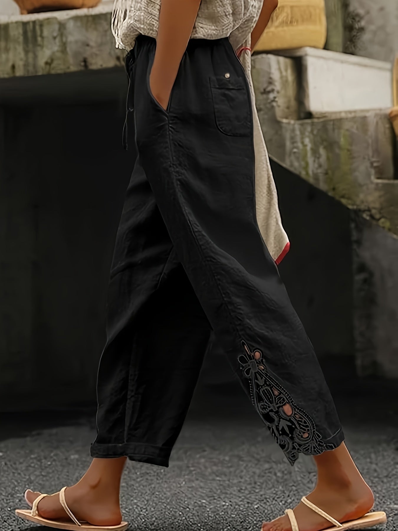 Person wearing black pants with lace details and a white top, standing on a stone surface.