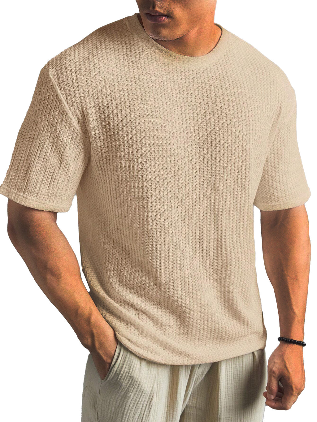 Man wearing a beige textured t-shirt and light-colored pants on a white background