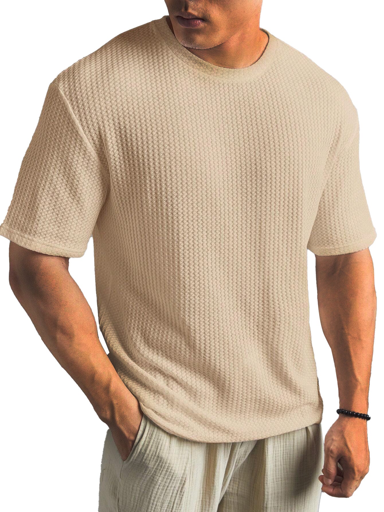 Man wearing a beige textured t-shirt and light-colored pants on a white background