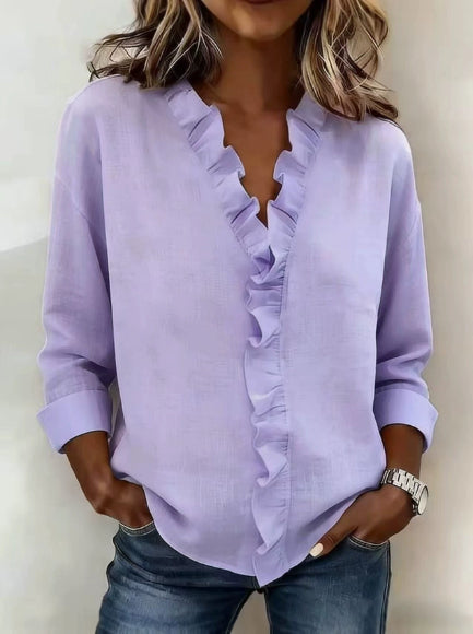 Woman wearing a light purple blouse with ruffle details and blue jeans against a neutral background