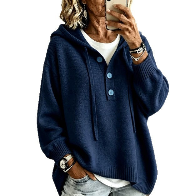 A woman wearing a navy blue knit hooded sweater with a three-button placket over a white undershirt, paired with light-wash jeans. She is holding a smartphone to take a mirror selfie against a plain white background.