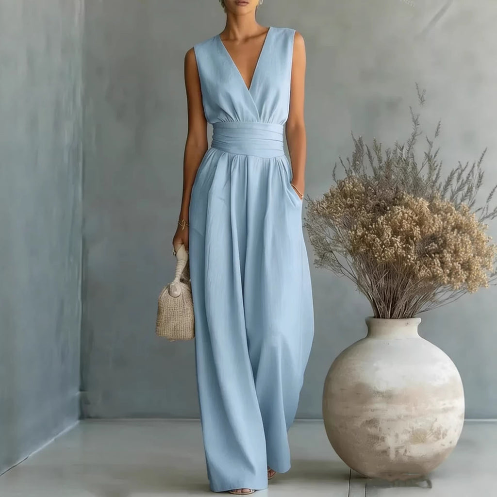 Woman in a light blue dress standing next to a vase with dried flowers against a gray wall.