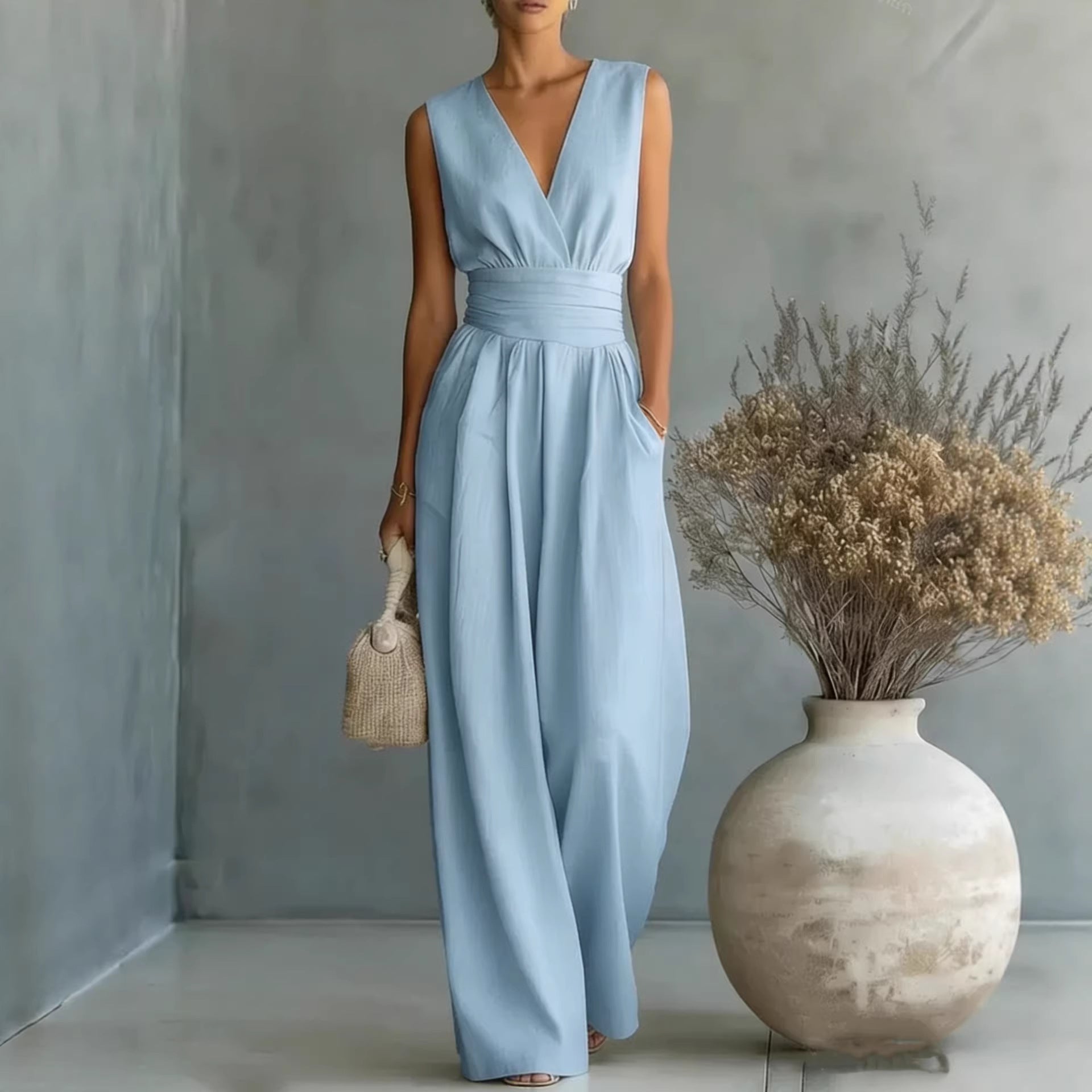 Woman in a light blue dress standing next to a vase with dried flowers against a gray wall.