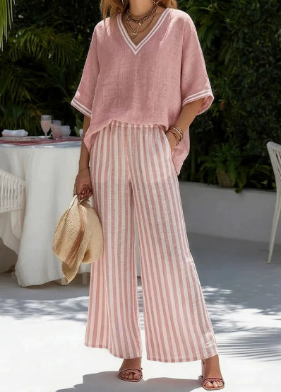 Woman in a pink outfit with striped pants standing outdoors near a table.