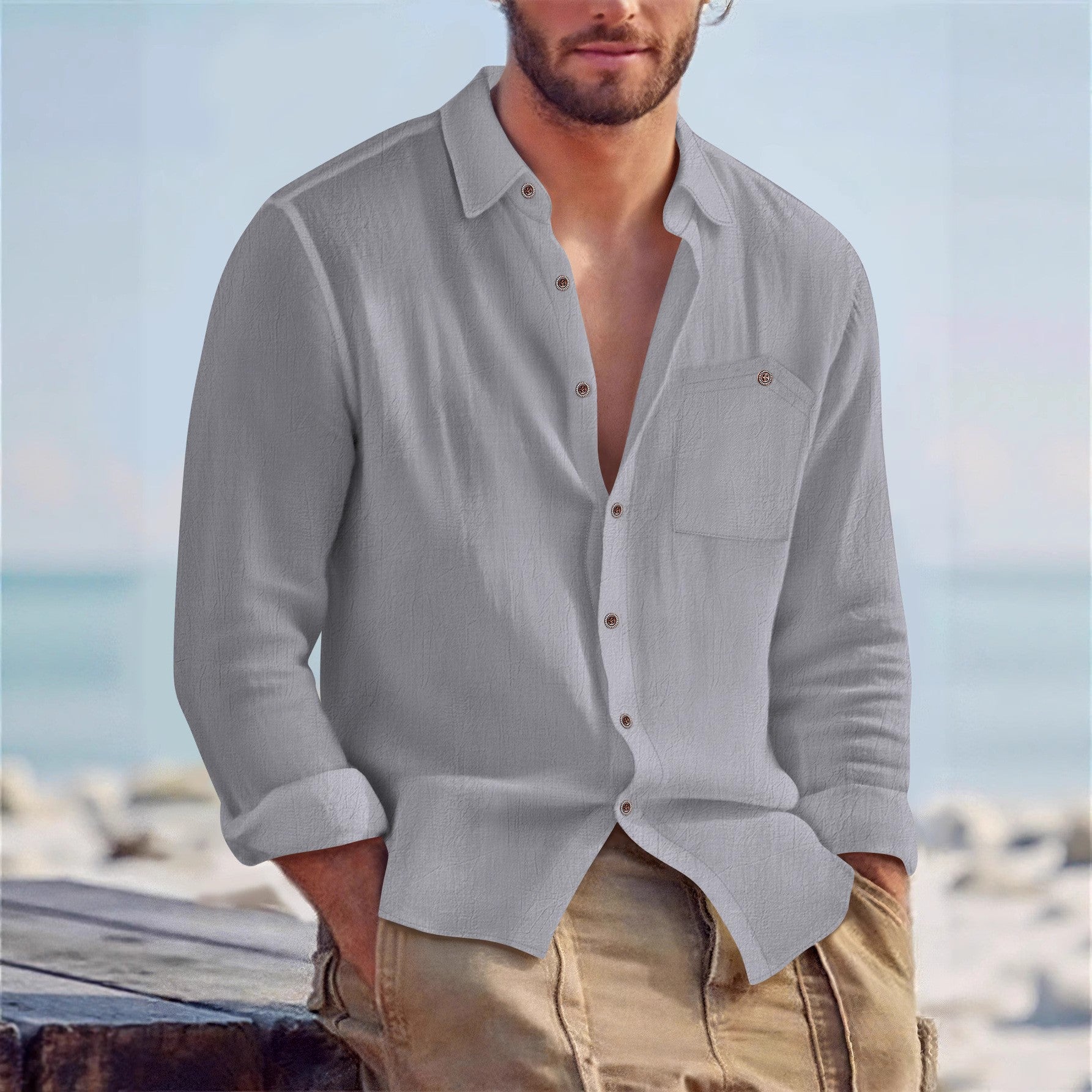 Man wearing a light gray button-up shirt with rolled-up sleeves and beige pants against a beach background.
