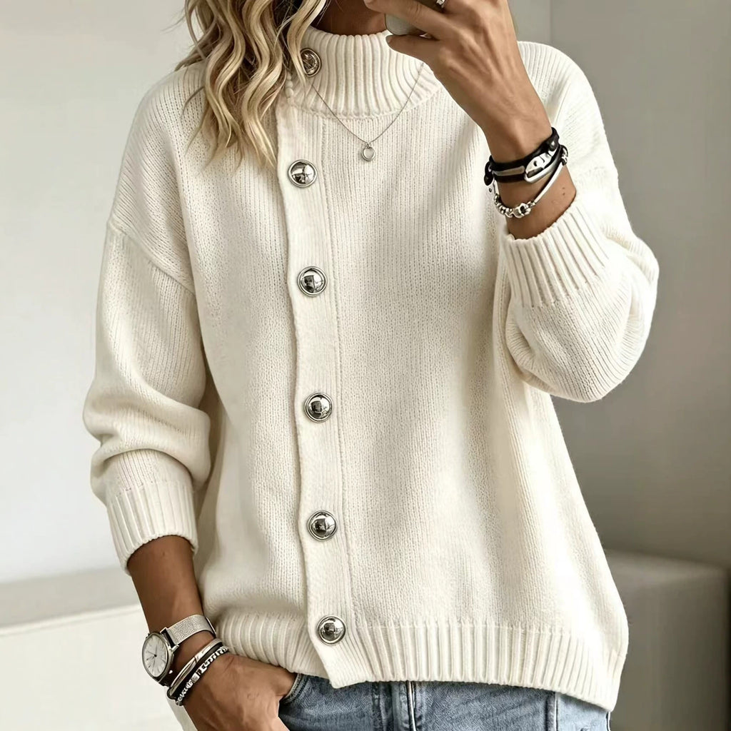 A woman wearing a cream-colored, long-sleeve knit cardigan sweater with silver-tone buttons, paired with blue jeans and accessorized with bracelets and a necklace.
