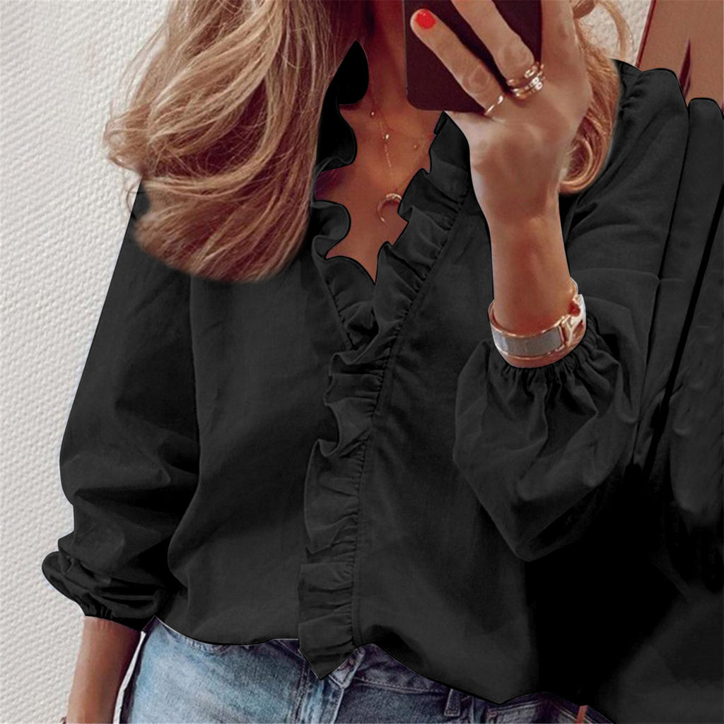 Person wearing a black ruffled blouse with a plain background