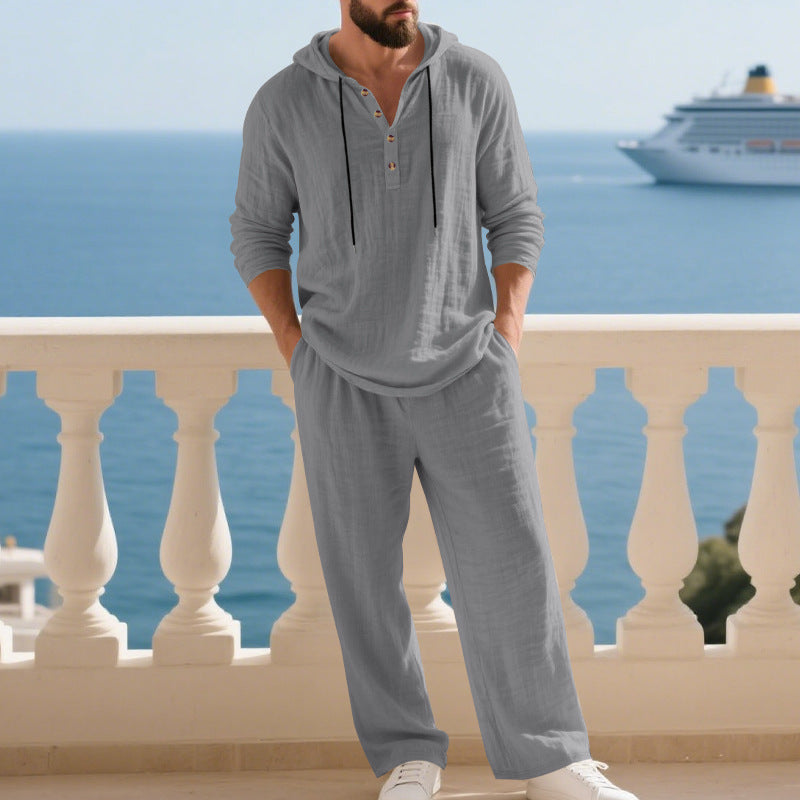Man wearing a gray hoodie and pants standing on a balcony with ocean and cruise ship in the background