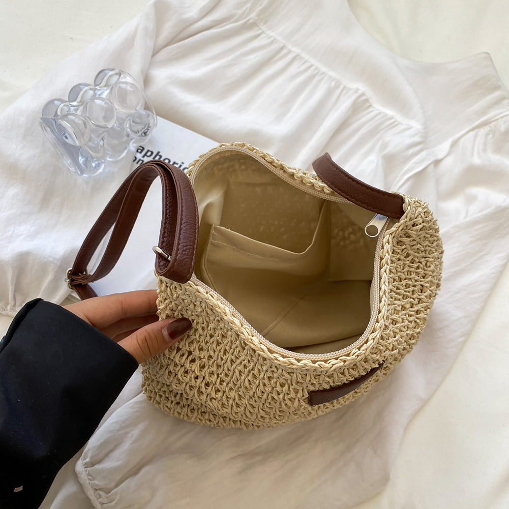 Hand holding a woven handbag with brown leather straps on a white surface