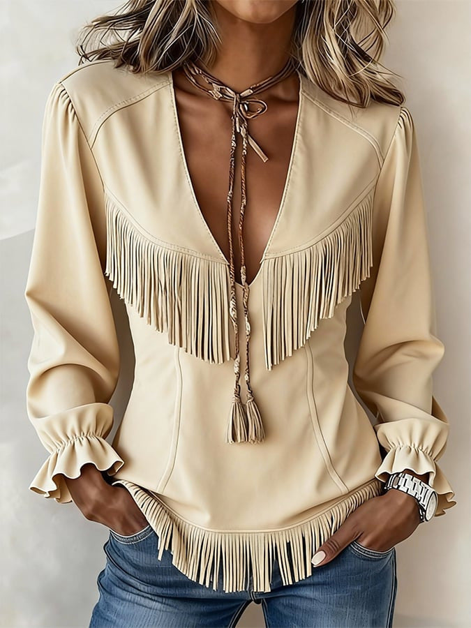Beige blouse with fringe details and blue jeans on a neutral background