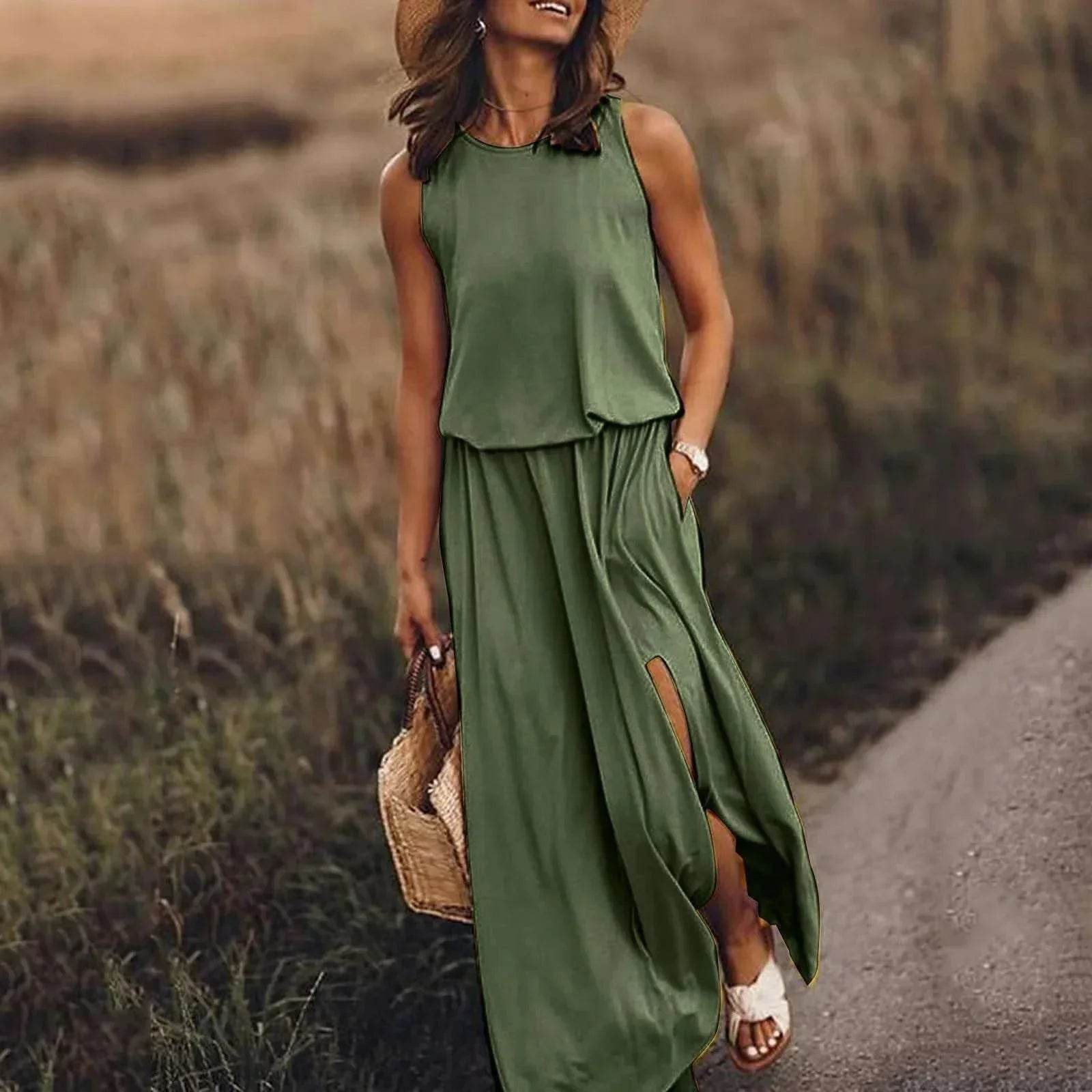Woman in a sleeveless green maxi dress and straw hat walking outdoors, holding a woven bag