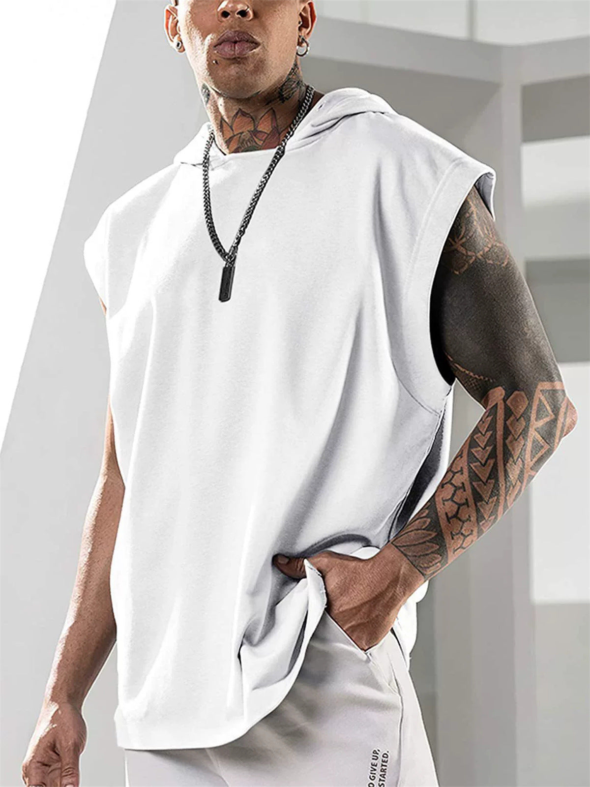 Person wearing a white sleeveless hoodie and white pants with tattoos on arms and neck.