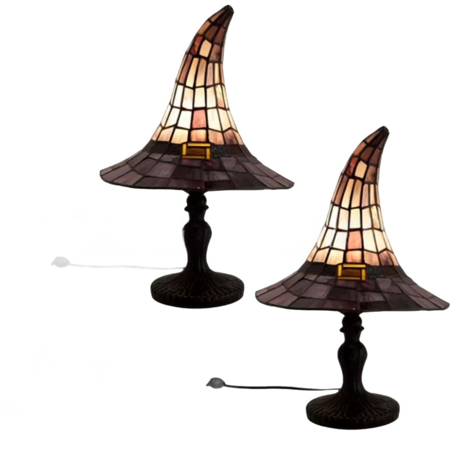 Two witch hat table lamps with stained-glass style shades in warm amber, cream, and brown tones, mounted on dark metal bases with visible cords on a white background.