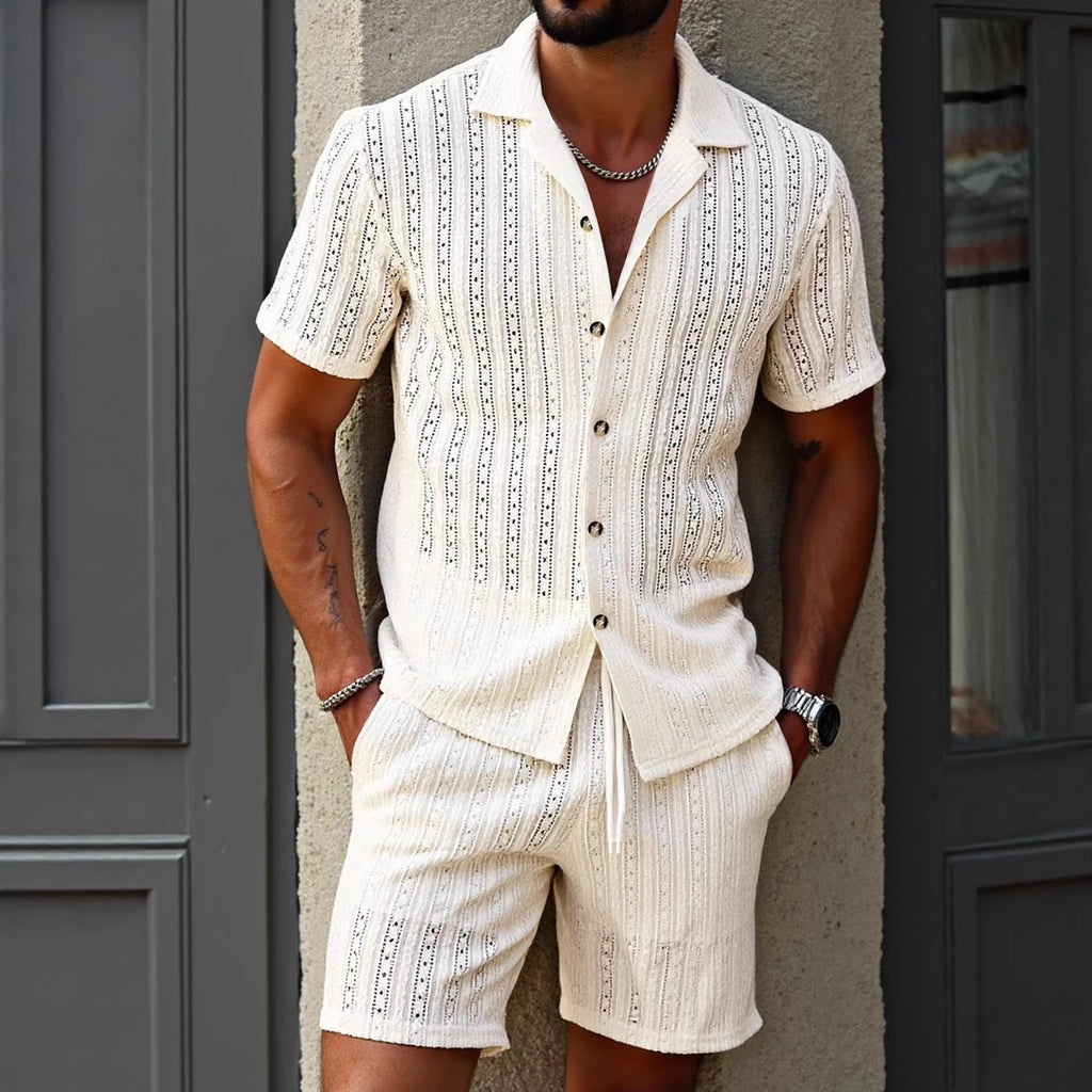 Man wearing a white embroidered shirt and shorts set against a gray wall.
