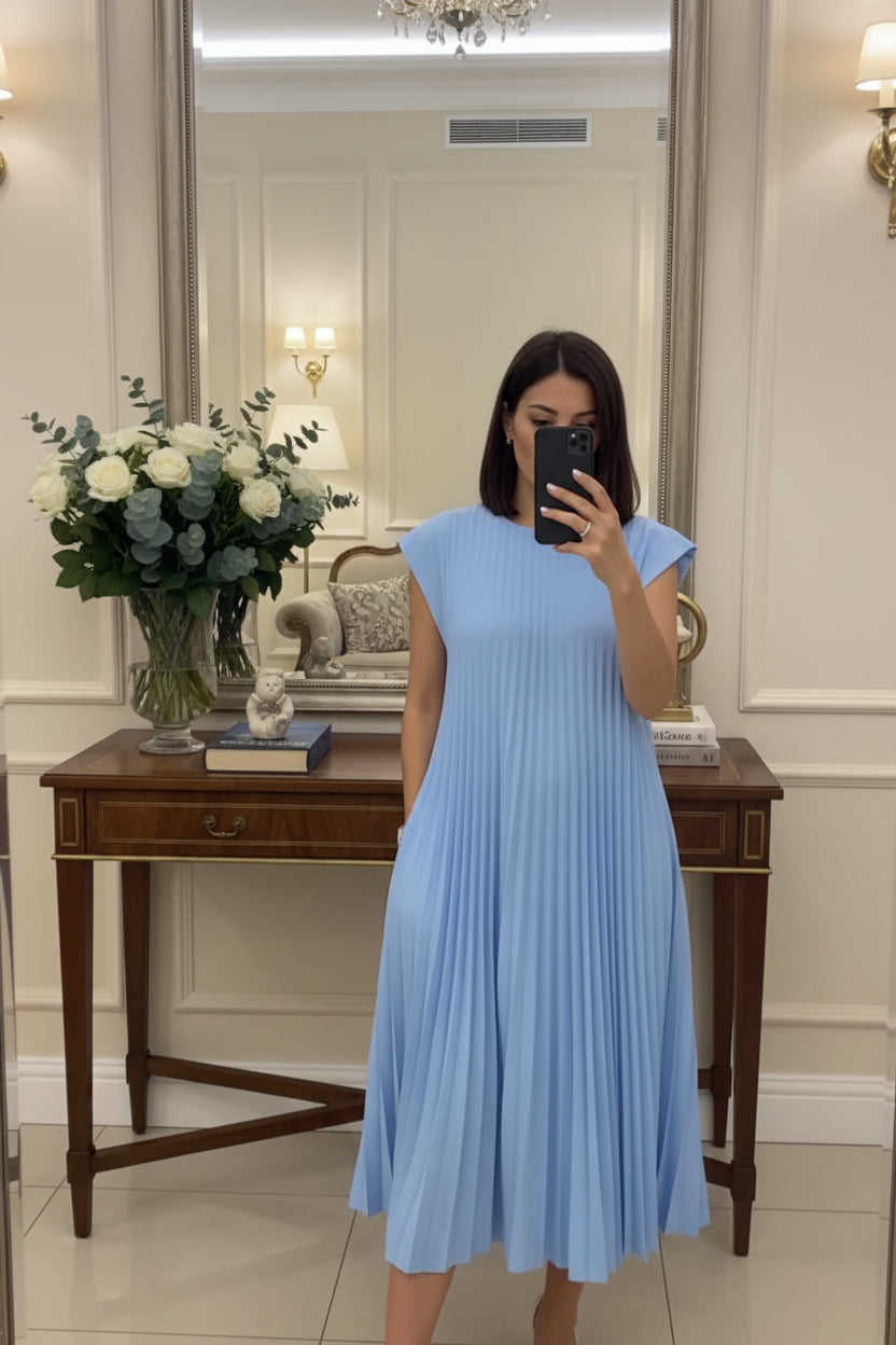 Person wearing a light blue pleated dress in a room with decor elements.