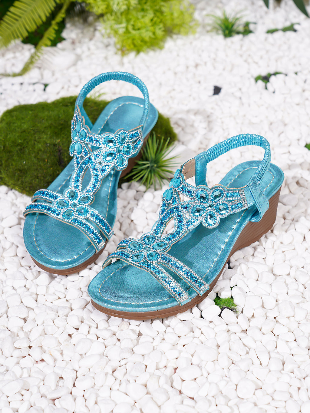 Pair of blue sandals with embellishments on a white pebble surface.