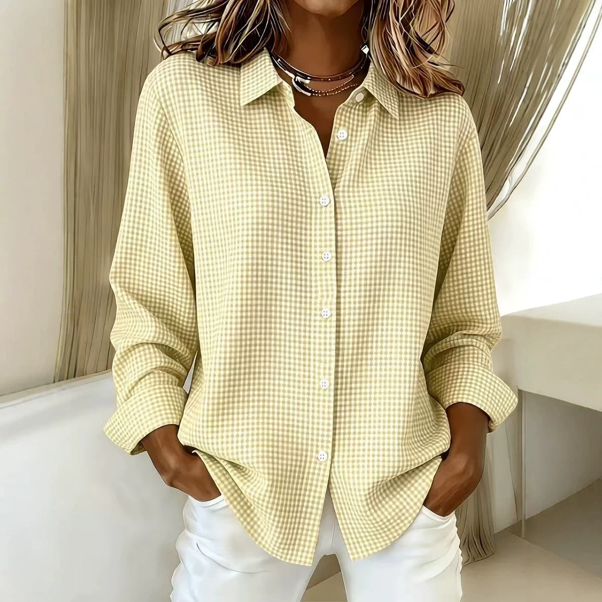 A woman wearing a pale yellow and white gingham button-up shirt with white pants, standing in a brightly lit indoor setting.