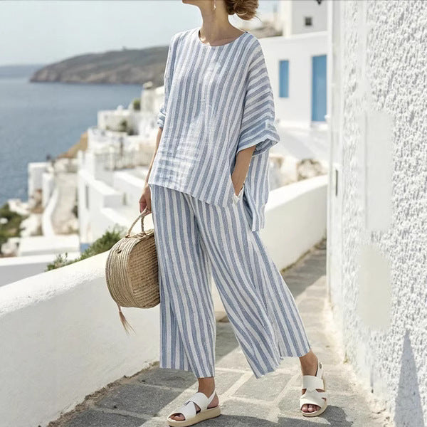Person wearing a blue and white striped outfit standing on a white pathway with ocean view.