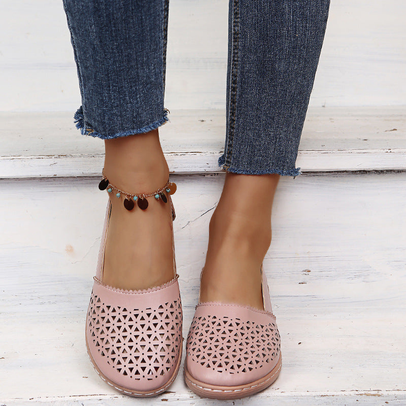 Pink perforated shoes worn with rolled-up jeans on a light wooden floor.