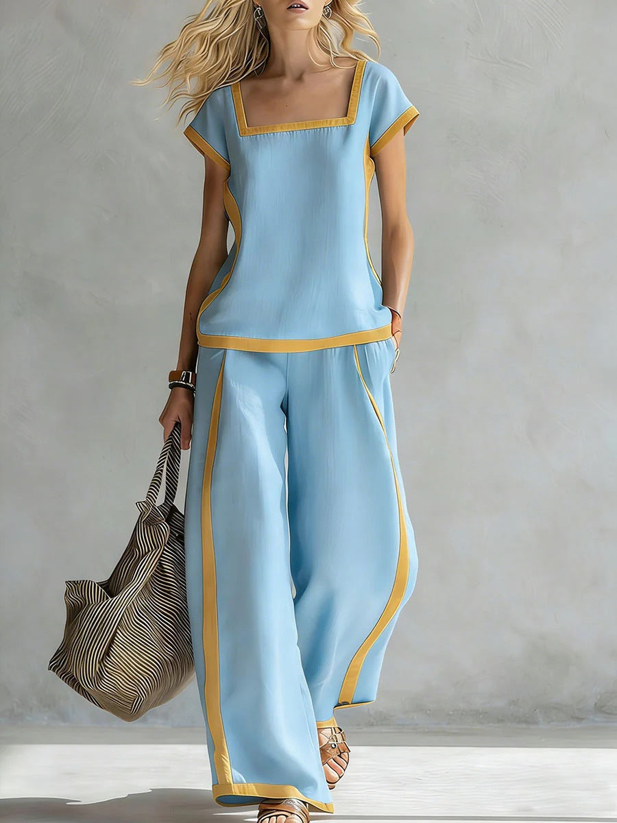 Woman wearing a light blue outfit with yellow accents, holding a striped bag against a neutral background.