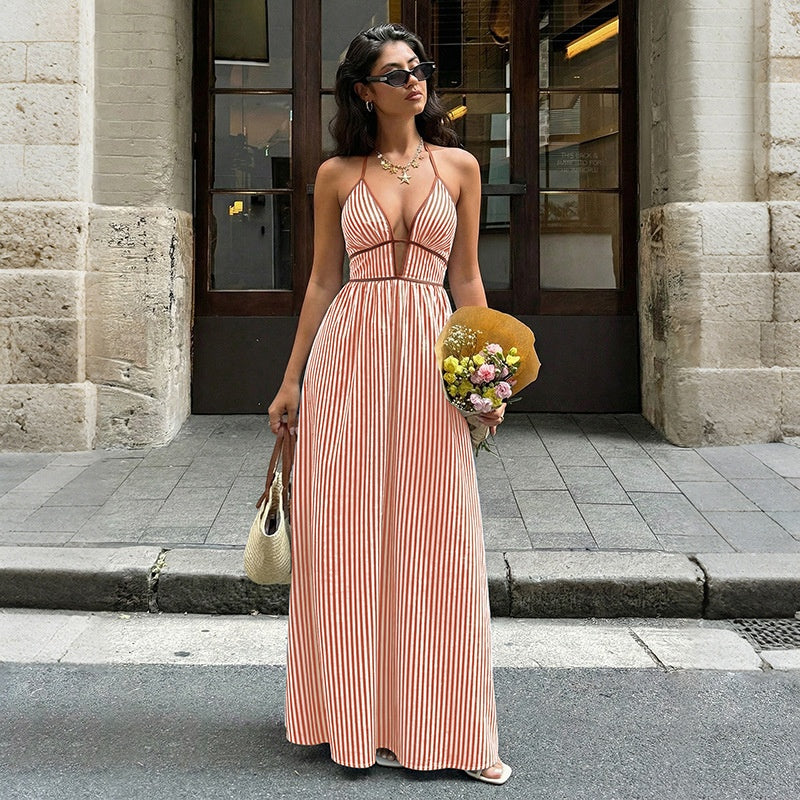 Woman in a striped dress holding flowers and a yellow bag on a city street.