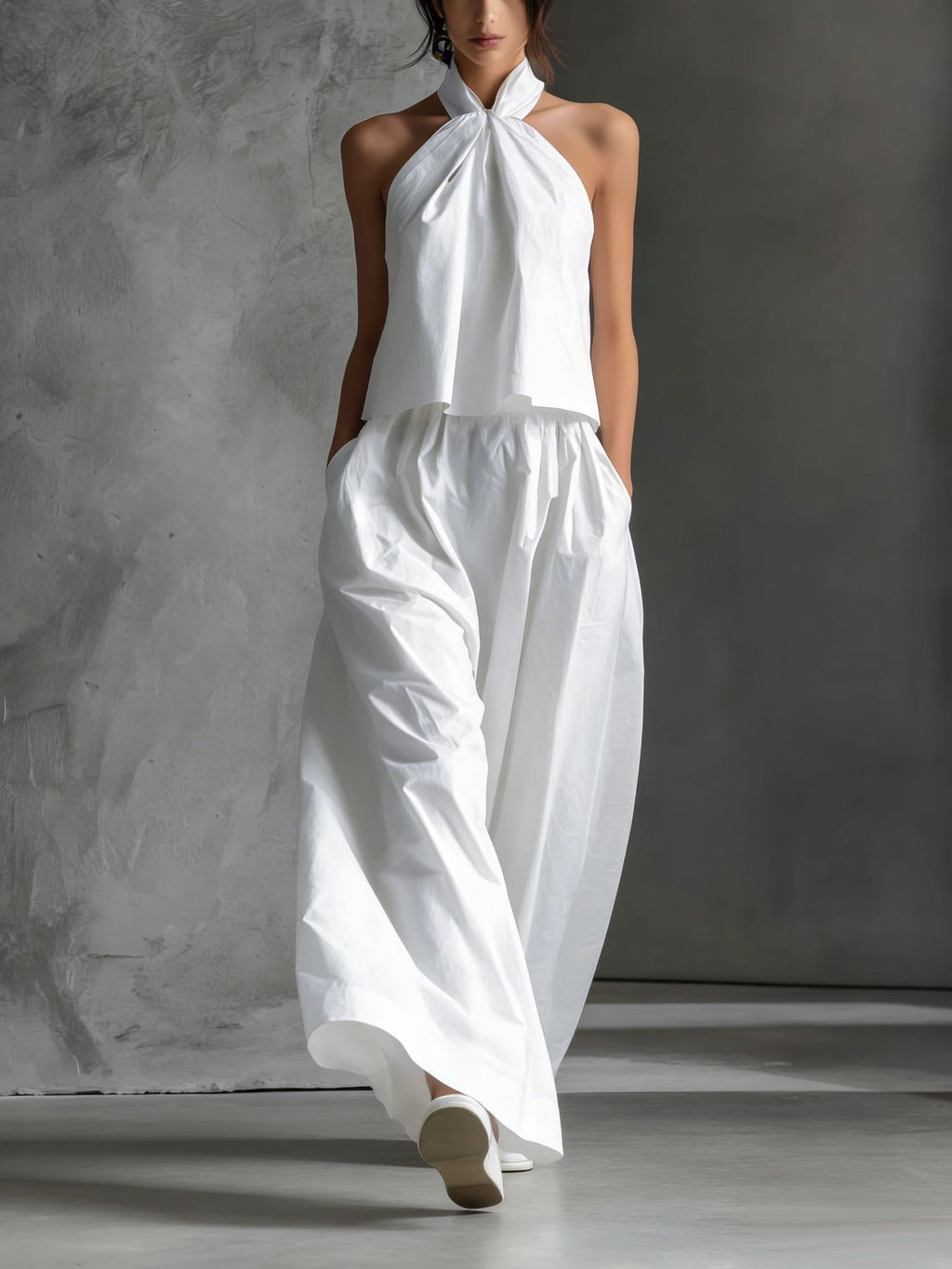 Person wearing a white halter top and wide-leg pants against a gray background