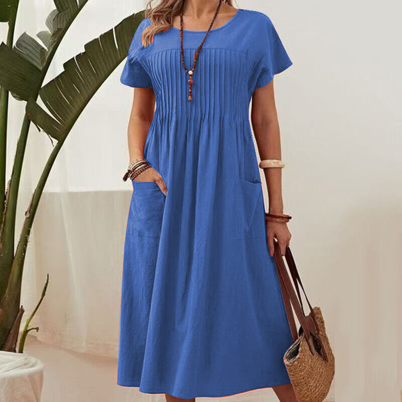 Woman wearing a blue dress holding a straw bag indoors with a plant in the background