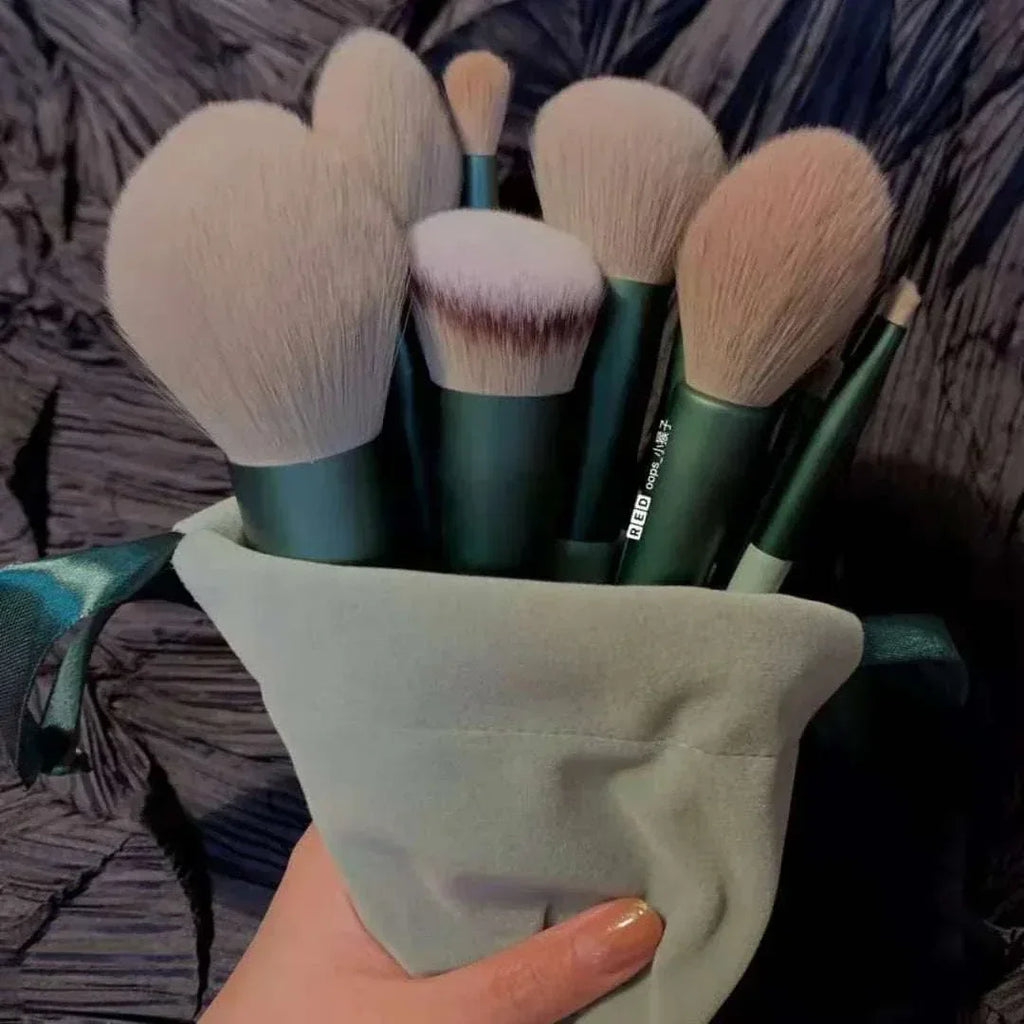 Set of soft makeup brushes with green handles in a light pouch, held by a hand