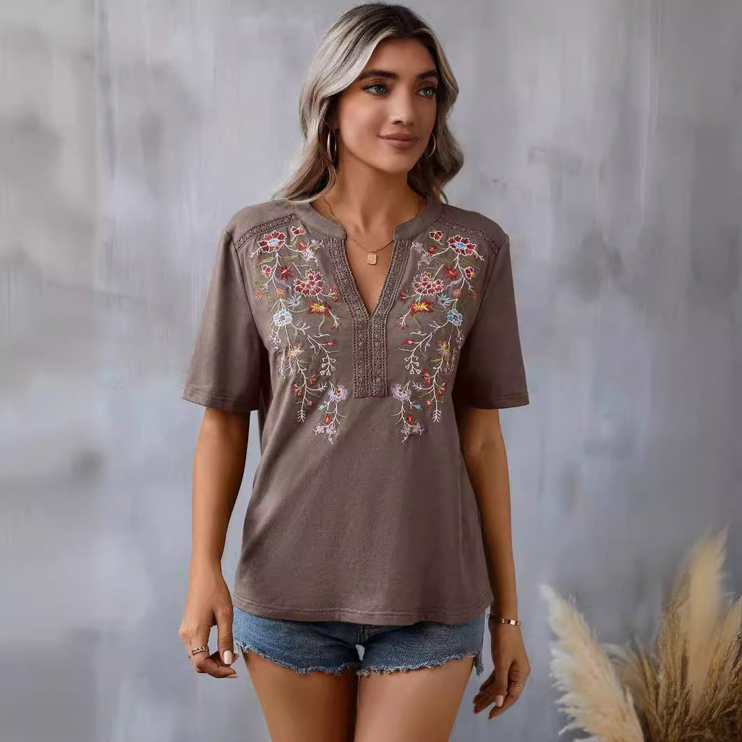 Woman wearing a brown embroidered top with denim shorts against a gray background