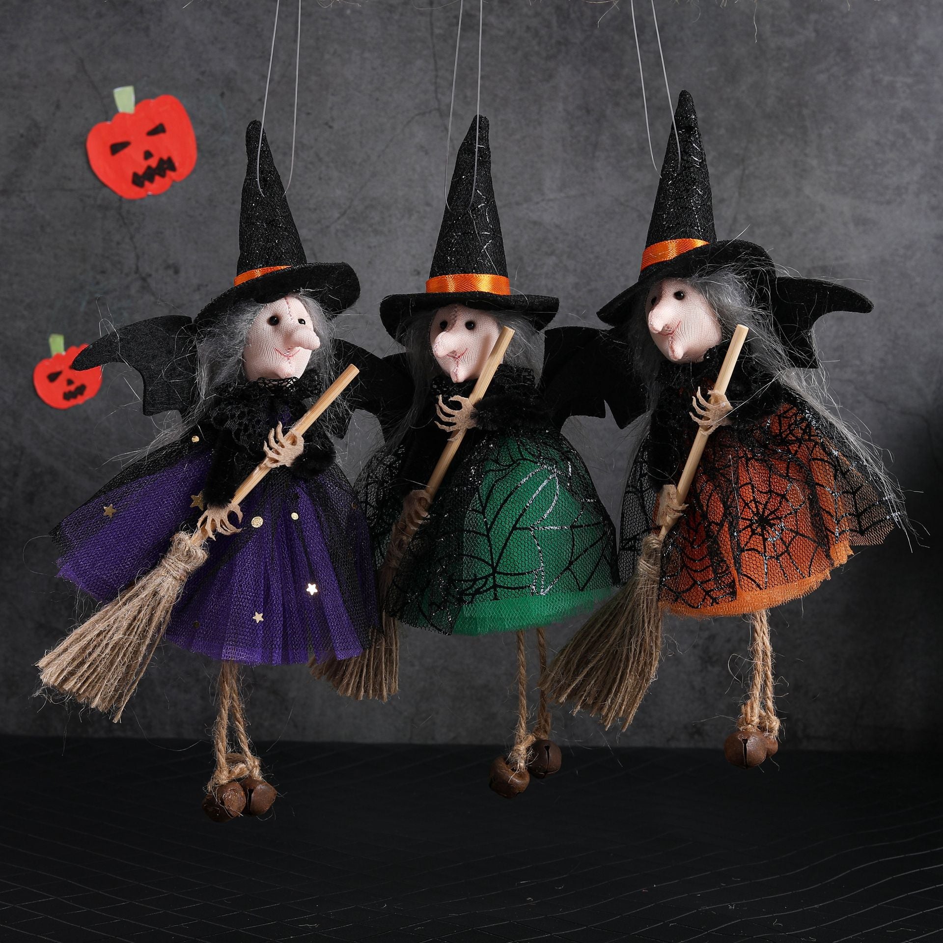 Three witch figurines with brooms and colorful dresses on a dark background
